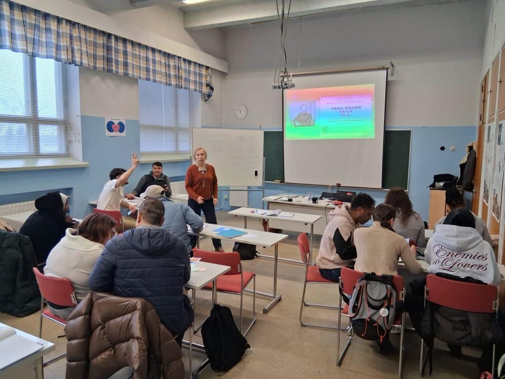 Classroom scene with students at desks a presenter in front and a colorful slide projected on the screen  Kainuun Opisto